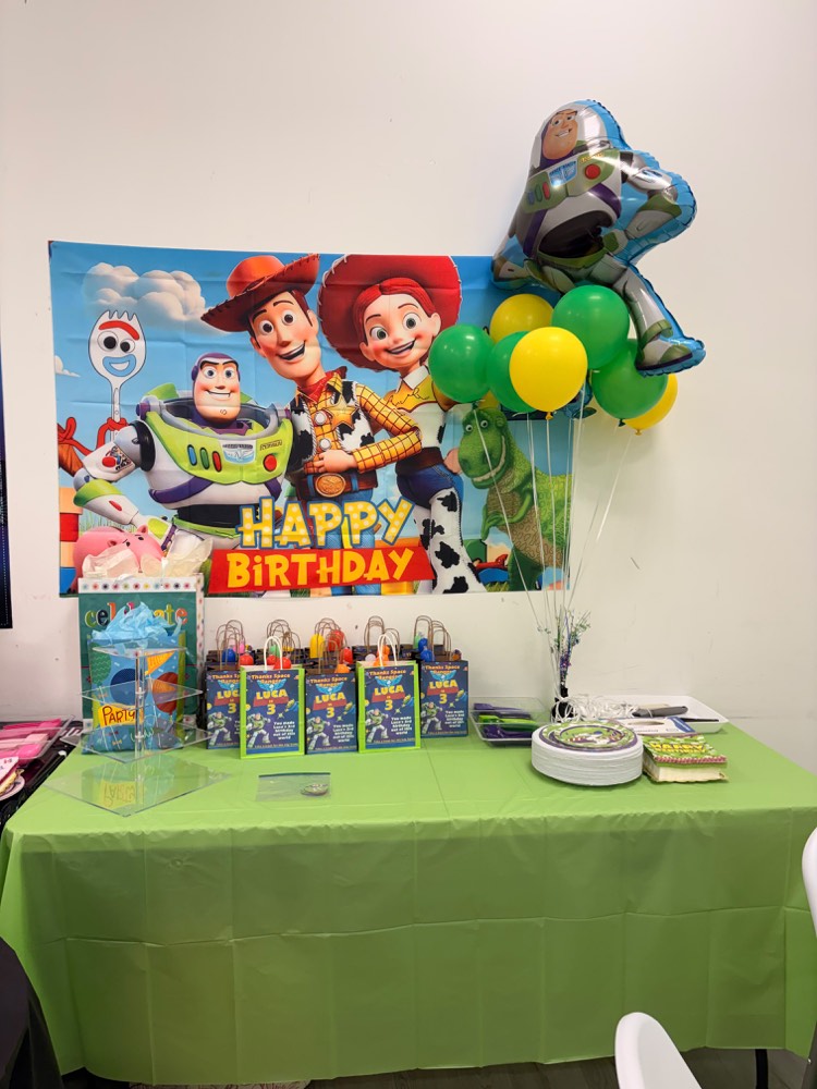 Toy Story party setup: Buzz and Woody backdrop, Buzz Lightyear foil balloon, green tablecloth and themed goodie bags