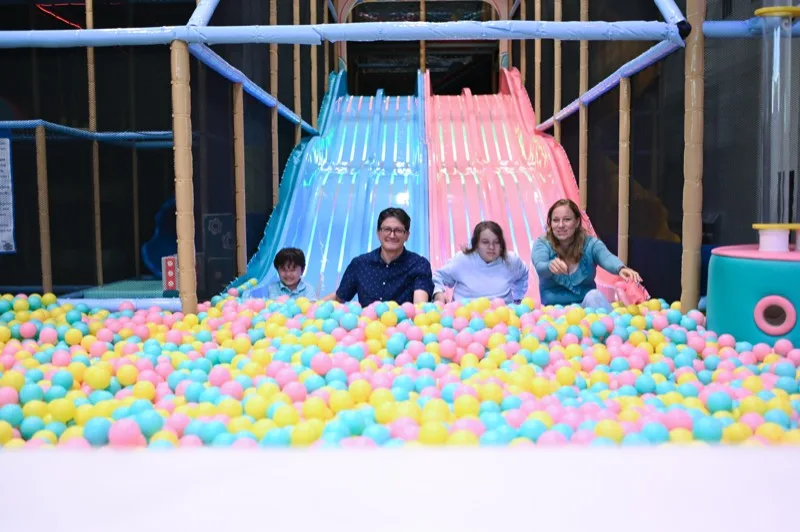 A family sliding down into the ball pit